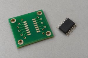 Bare PCB with exposed component pads and a loose leaded integrated circuit beside it