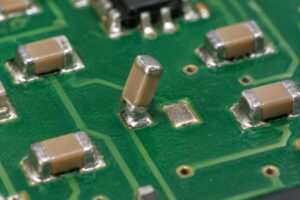 Illustrative chip capacitor standing on one termination beside its empty PCB pad